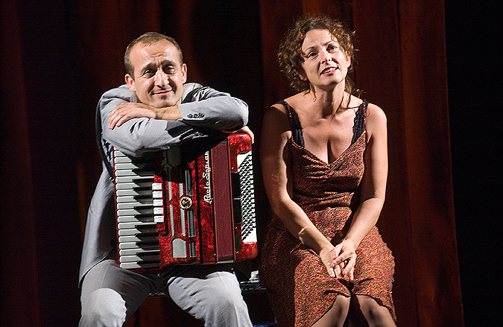 Scena dallo spettacolo Senza Carità. Giorgio e Helena sono seduti su una panchina. Giorgio ha una fisarmonica appoggiata sulle gambe, a cui lui stesso si appoggia a braccia conserte. Guardano l'orizzonte con sguardi trasognati.