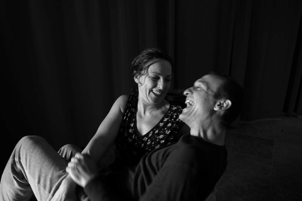 Foto in bianco e nero. Helena è seduta, con Giorgio in braccio. Entrambi ridono guardandosi.