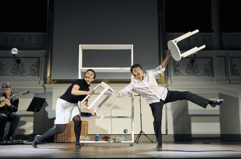 Un attore e un'attrice sul palco durante lo spettacolo, in equilibrio, con degli sgabelli in mano