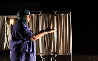 Teresa, fotografata a mezza figura, di lato, vestita con divisa e cuffia, mentre si mette dei guanti monouso.