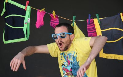 Primo piano di Luca. Dietro di lui un filo con il bucato steso, a cui è pinzato, con una molletta, anche il collo della maglietta che ha addosso, apparendo steso anche lui stesso.