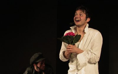 Piano americano di Fabio, in camicia bianca, con un mazzo di fiori in mano, con espressione felice.