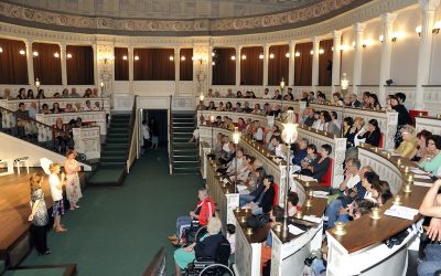 Foto laterale del pubblico durante la presentazione dello spettacolo. Sulla sinistra, appena sotto il palco, il team presenta lo spettacolo.