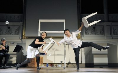 Un attore e un'attrice sul palco durante lo spettacolo, in equilibrio, con degli sgabelli in mano