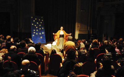 Grandangolo della sala durante lo spettacolo. Si vedono le prime cinque file di pubblico che guardano, al centro della scena, la lavandaia, in piedi, con le braccia aperte.