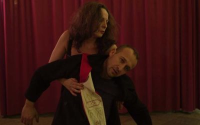Giorgio e Helena sono nel mezzo di una danza espressiva. Helena, dietro Giorgio, lo regge da sotto le braccia e Giorgio si accascia.